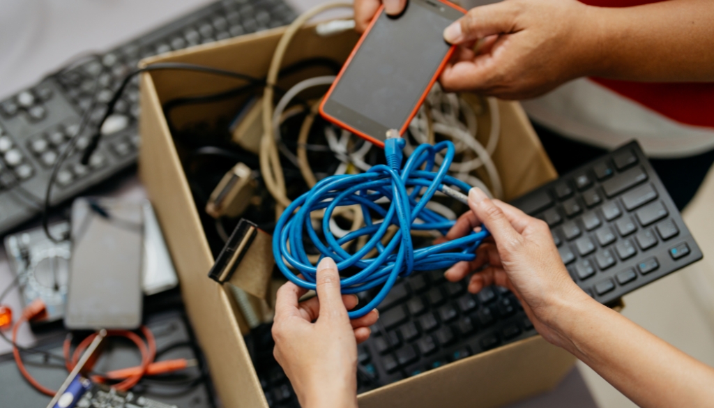 People putting old electronics into a cardboard box to simplify the recycling process.|Various electronics in a box being recycled.