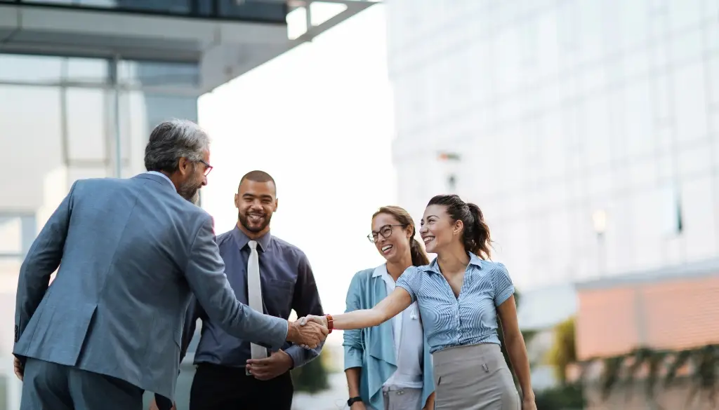 Business partners demonstrating service excellence while shaking hands outside of an office building.|Business partners shaking hands outside of an office building.