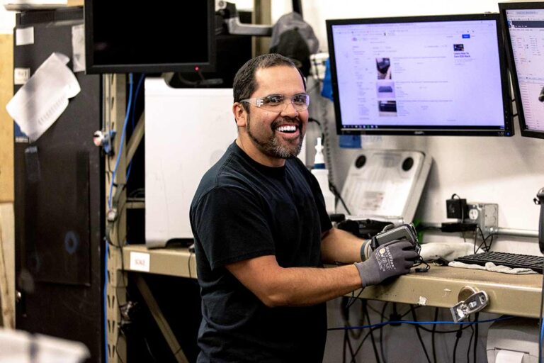 A Dynamic Lifecycle Innovations technician standing and smiling at a workstation.