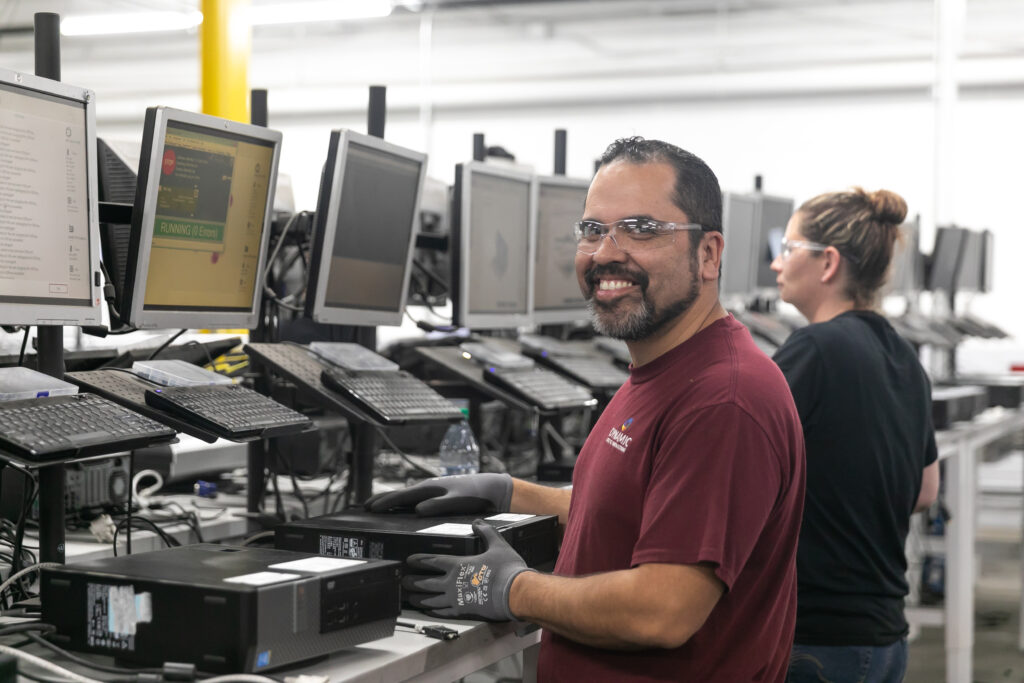 A Dynamic Lifecycle Innovations technician standing and smiling at their workstation.