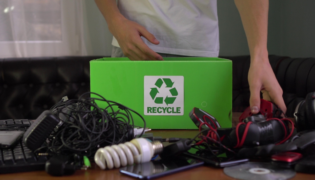 A man sorting through a table full of corporate electronics to place in an e-waste recycling box.