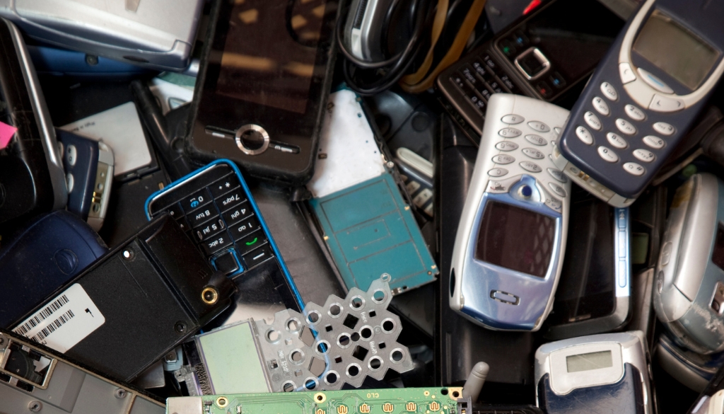 Small IT Assets, including vintage cell phones and computer chips are piled in a recycling bin.