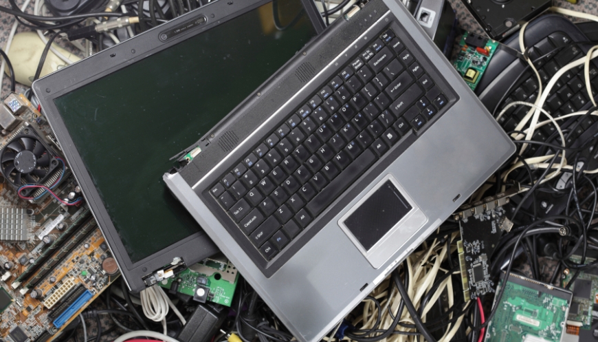 A pile of e-waste containing a broken laptop, motherboards, cords, and drives.