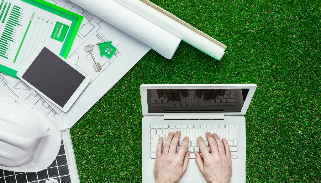 Man working on a laptop next to a tablet, and a printed sustainability report chart.