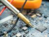 Close-up of a technician using a soldering iron on a hard disk drive during electronics refurbishment.