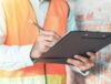 Man wearing an orange safety vest checking off items on a clipboard for a company's ITAD process.