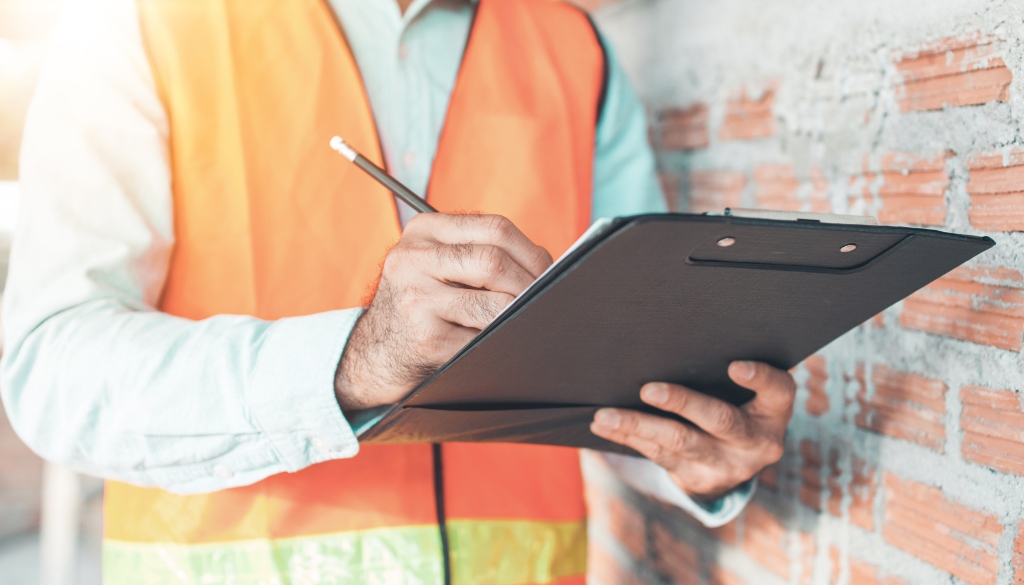 Man wearing an orange safety vest checking off items on a clipboard for a company's ITAD process.