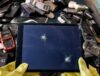 Person wearing gloves holding a broken tablet above old electronics.