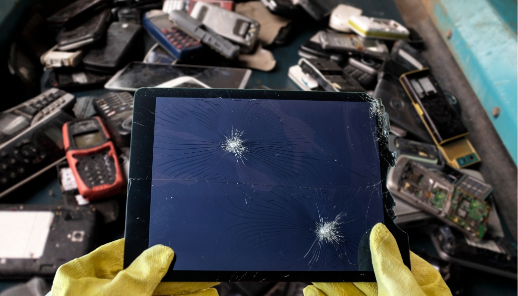 Person wearing gloves holding a broken tablet above old electronics.