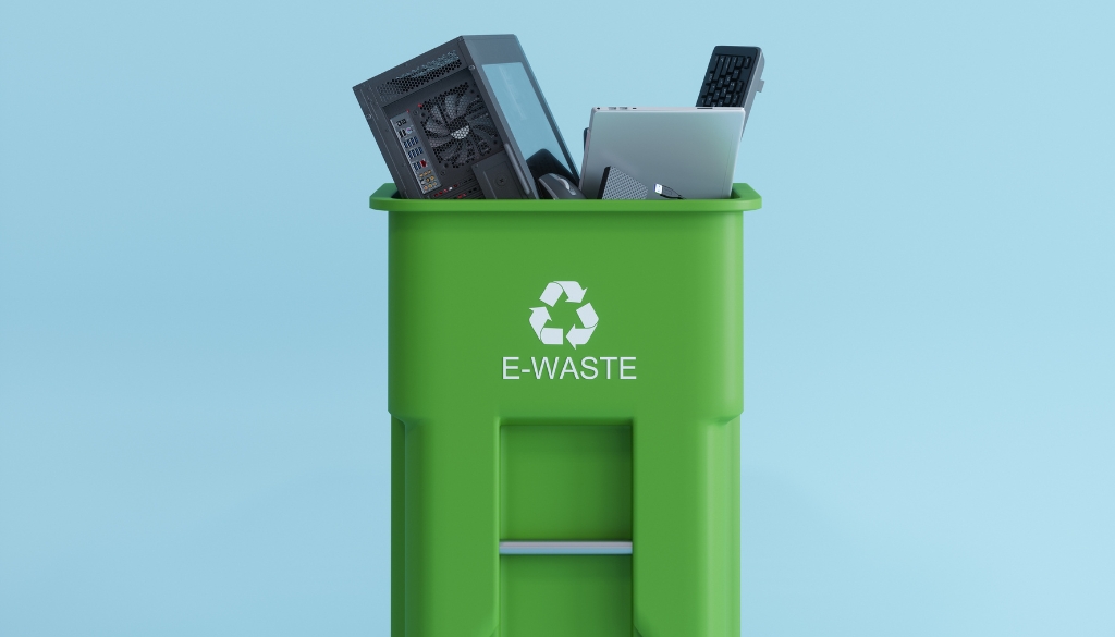 Computer, monitor, and various electronics in an overflowing green recycle bin.