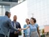 Business partners demonstrating service excellence while shaking hands outside of an office building.