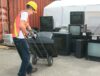 Worker moving TVs on a dolly to be recycled.