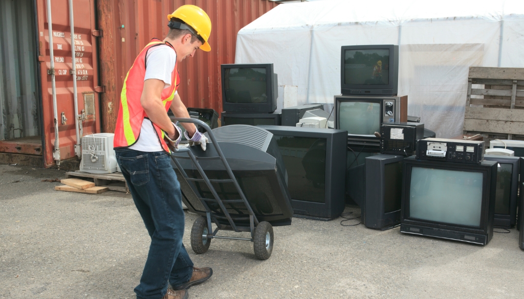 Worker moving TVs on a dolly to be recycled.