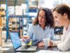 2 Business women look at a laptop in an electronics recycling facility.