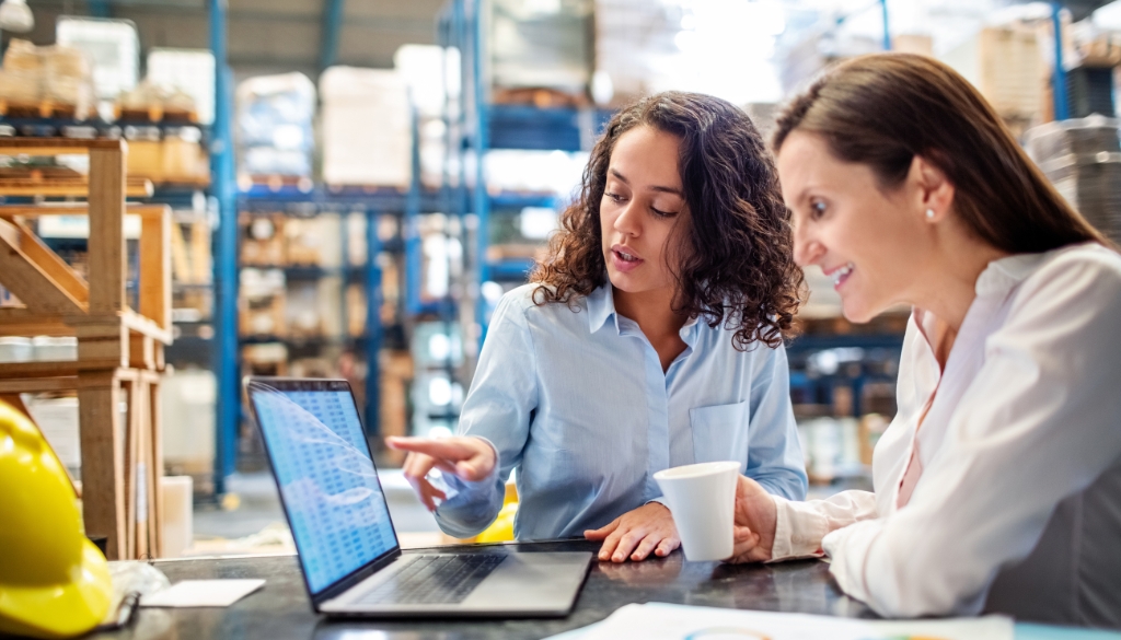 2 Business women look at a laptop in an electronics recycling facility.