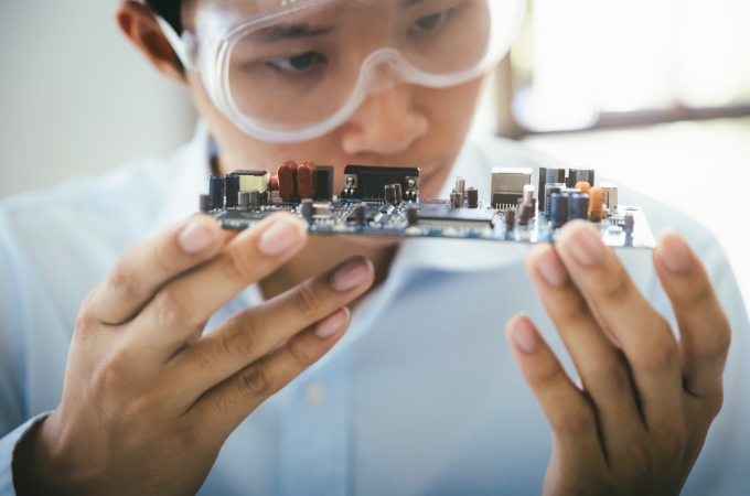 An electronic worker wearing safety goggles viewing an integrated circuit.